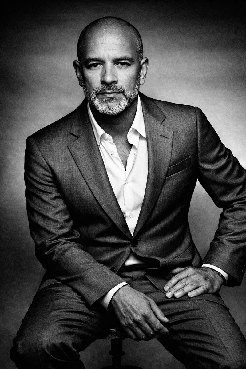 Pacho Sánchez sentado en un estudio, traje oscuro y camisa blanca abierta, retrato en blanco y negro