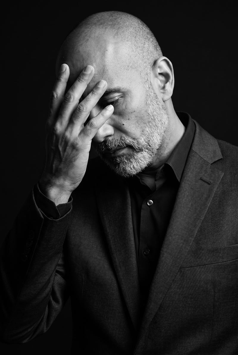 Pacho Sánchez con la mano en la frente, gesto de cansancio, retrato en blanco y negro sobre fondo negro